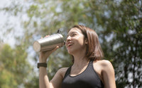 Femme dehors qui bois dans une bouteille isotherme.