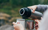 Personne qui sert du thé dans deux mug, d'un grand thermos en onix.