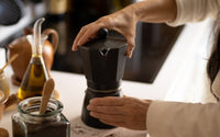 Cafetière italienne noire tenue par une femme qui la dévisse.