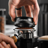 Anneau Noir Dosage Café Magnétique 58mm, un barista l'installe sur un porte filtre à café.