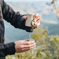 Cafetiere Portable avec Adaptateur pour Capsules, avec un homme se servant un café dans la nature.