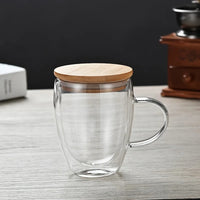 Mug Double Paroi en Verre avec Poignée et Couvercle, sur une table grise.