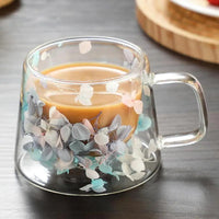 Mug Double Paroi en Verre avec Poignée et Design Fleuri, sur une table grise.