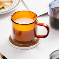 Mug Double Paroi en Verre avec Poignée Orange, sur une table blanche.