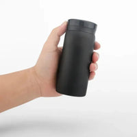 Mug Thermos Café Petit Format en Acier Inoxydable, de couleur noir, dans une main, sur un fond blanc.