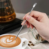 Stylo en acier inoxydable pour latté art, utilisé par une barista pour faire un dessin dans un café