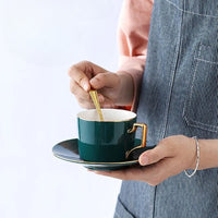 Tasse à Café avec Support en Céramique et Élégante, de couleur verte, tenue dans une main.
